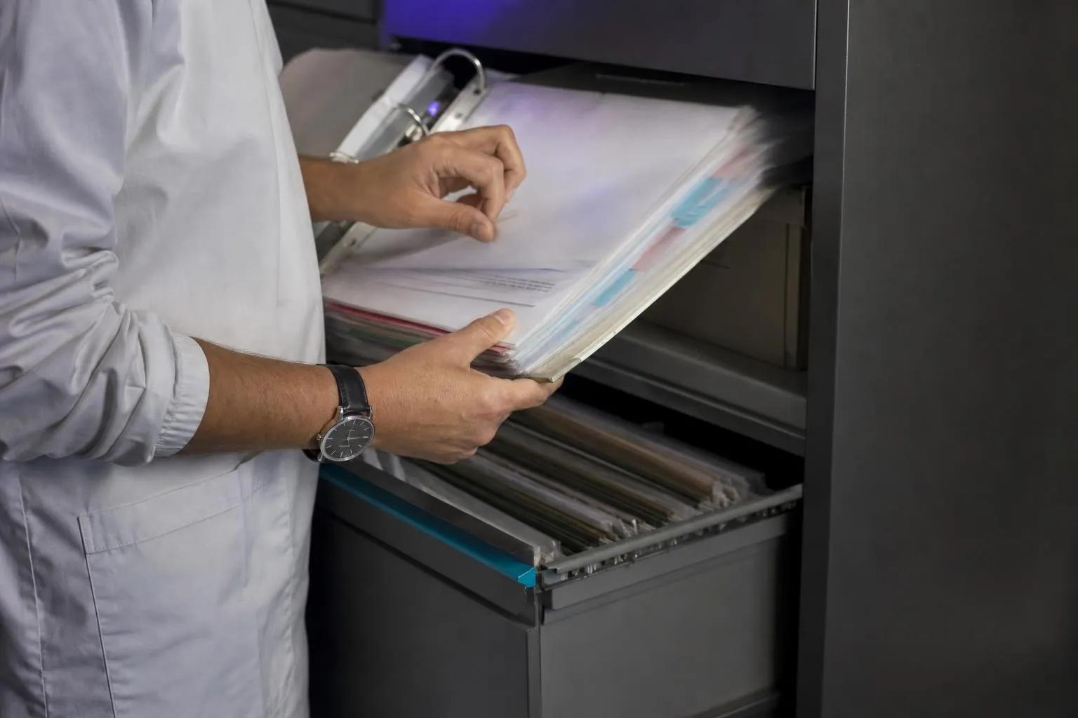 Mains feuilletant rapidement les intercalaires d’un classeur épais devant un tiroir d’archives ouvert