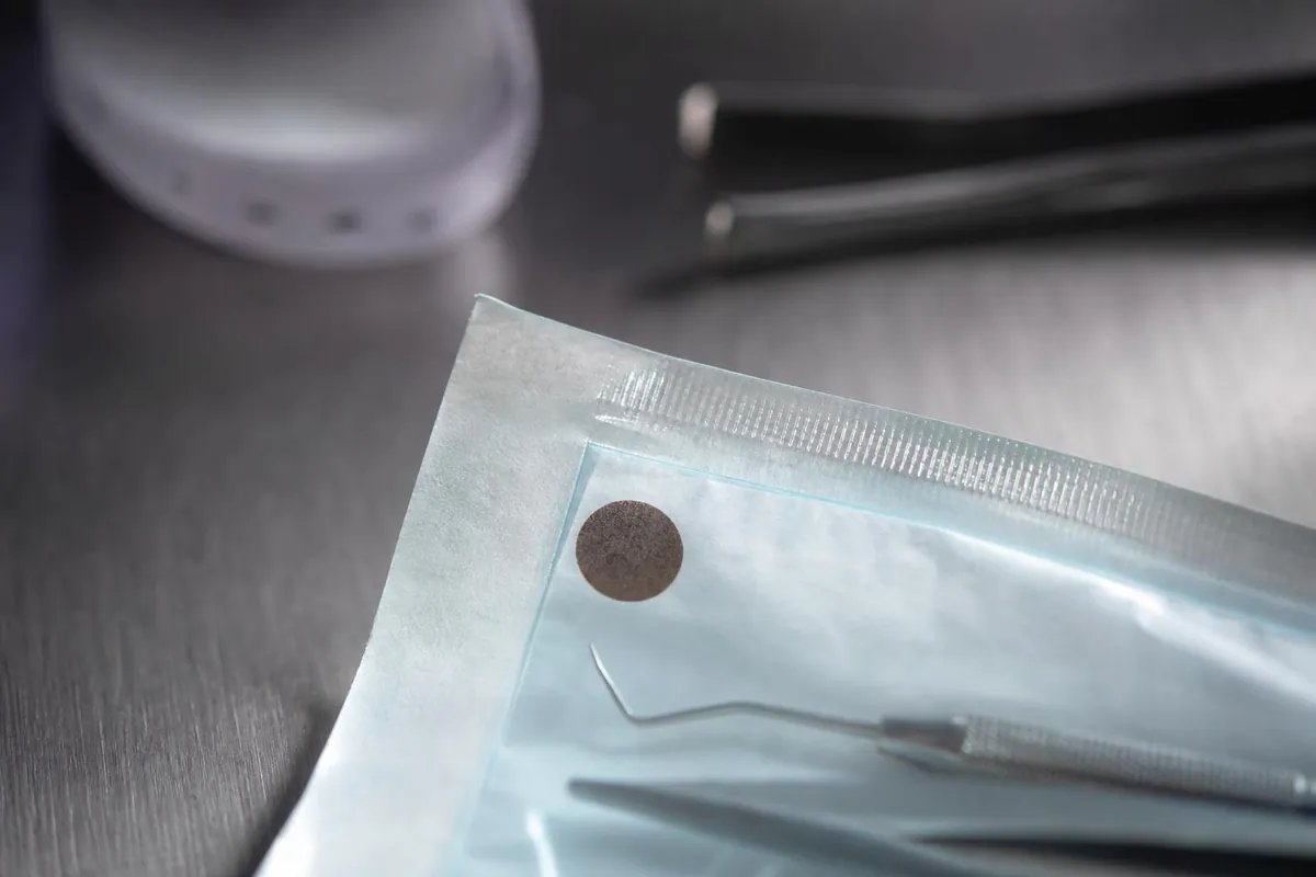 Gros plan sur le coin d'un sachet de stérilisation scellé avec indicateur de passage viré, posé sur un plan de travail en inox